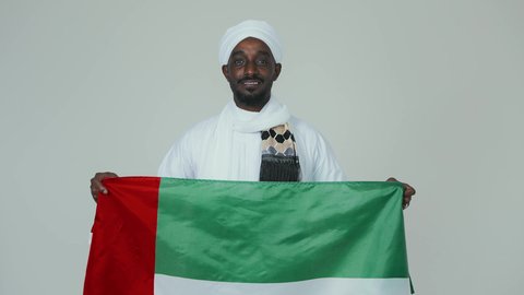 ايماءات الفخر والسرور، حمل العلم السوداني بفخر،الاحتفال بالاستقلال ١ يناير، استذكار اليوم الوطني السوداني ١٩٥٦ م، حب الوطن والاعتزاز به، بورتريه مقرب لرجل عربي سوداني يرتدي الجلابية والشال والعمامه البيضاء يقف بثقة واستقامة، خلفية بيضاء