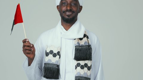 ايماءات السعادة والسرور، مفهوم الحب و الانتماء للبلاد, الأعياد و المناسبات الوطنية,  الاحتفال باليوم الوطني الإماراتي 2 ديسمبر, بورتريه لرجل عربي سوداني يرتدي العمامة والجلابية والشال يحمل علم الإمارات العربية المتحدة, خلفية بيضاء