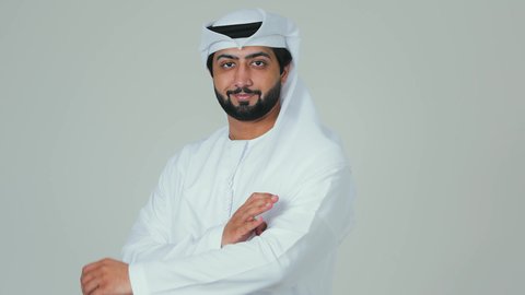الاناقة و الاهتمام  بالمظهر الخارجي ، الوقوف بايدي متقاطعة ، بورتريه مقرب لرجل عربي خليجي اماراتي يرتدي الكندورة و الغترة ينظر الى الكاميرا بايماءات الثقة بالنفس ، خلفية بيضاء