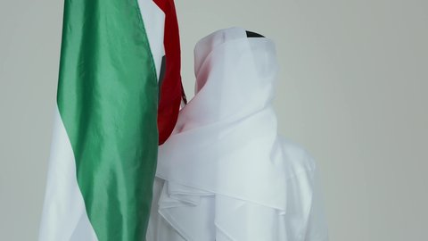 مفهوم الحب و الانتماء للبلاد, الأعياد و المناسبات الوطنية,  الاحتفال باليوم الوطني الإماراتي, بورتريه من الخلف لرجل عربي خليجي إماراتي يرتدي الكندورة والغترة البيضاء يقوم بوضع علم الإمارات العربية المتحدة, خلفية بيضاء