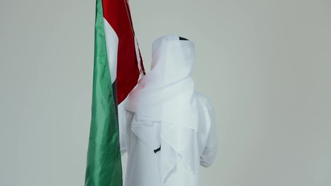 الأعياد و المناسبات الوطنية,  الاحتفال باليوم الوطني الإماراتي, مفهوم الحب و الانتماء للبلاد, بورتريه من الخلف لرجل عربي خليجي إماراتي يرتدي الكندورة والغترة البيضاء يقوم بوضع علم الإمارات العربية المتحدة, خلفية بيضاء