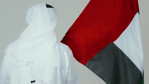 الأعياد و المناسبات الوطنية,  الاحتفال باليوم الوطني الإماراتي, مفهوم الحب و الانتماء للبلاد, بورتريه من الخلف لرجل عربي خليجي إماراتي يرتدي الكندورة والغترة البيضاء يقوم بوضع علم الإمارات العربية المتحدة, خلفية بيضاء