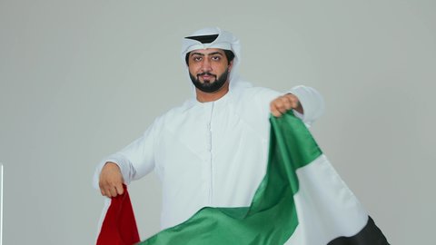 مفهوم الحب و الانتماء للبلاد, السعادة والسرور في المناسبات الوطنية، الاحتفال باليوم الوطني الإماراتي, الأعياد و المناسبات الوطنية,  بورتريه لرجل عربي خليجي إماراتي يرتدي الكندورة والغترة البيضاء يقوم بحمل علم الإمارات العربية المتحدة, خلفية بيضاء