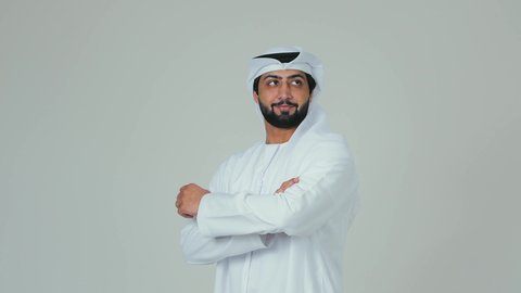 الوقوف بايدي متقاطعة ، الاناقة و الاهتمام  بالمظهر الخارجي ، بورتريه  لرجل عربي خليجي اماراتي يرتدي الكندورة و الغترة ينظر الى الكاميرا بايماءات الثقة بالنفس ، خلفية بيضاء
