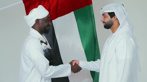 الاحتفال باليوم الوطني الاماراتي 2  ديسمبر ،اتفاقية عمل جديده بين الشركاء، صفقة جماعية مشتركة ناجحة،بورتريه  لرجل عربي اماراتي يرتدي الكندورة و الغترةيقوم بمصافحة رجل سوداني يرتدي الجلابية و العمامة و الشال،اتفاقيات بين البلدان ،تعارف و صداقات وعلاقات جديدة ، لفية بيضاء