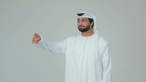 Pointing with the index finger at something specific, a portrait of an Emirati Gulf Arab man wearing a kandura and ghutrah, standing upright and pointing at something, standing confidently and paying attention to his appearance, white background.