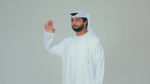 الوقوف بثقة والاهتمام بالمظهر الخارجي، ايماءات السرور والسعادة، بورتريه لرجل عربي خليجي اماراتي يرتدي الكندورة والغترة  يقف باستقامة ويقوم بإلقاء التحية العسكرية ،  خلفية بيضاء