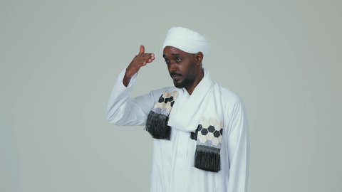 Raising the hand to try to see distant things, a love for exploration and adventure, a portrait of a Sudanese Arab man wearing a jalabiya and a turban, standing upright and looking at something, standing confidently and caring about his appearance, with a white background.