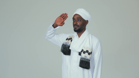 الوقوف بثقة والاهتمام بالمظهر الخارجي، ايماءات السرور والسعادة، بورتريه لرجل عربي سوداني يرتدي الجلابية ويضع العمامة والشال يقف باستقامة ويقوم بإلقاء التحية العسكرية ،  خلفية بيضاء