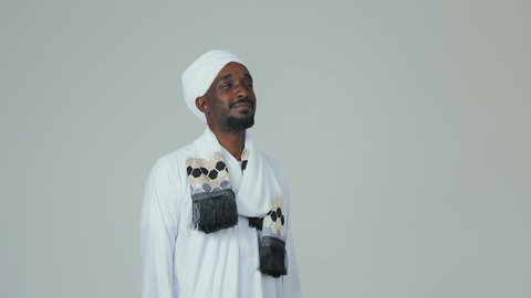 ايماءات السرور والسعادة، بورتريه لرجل عربي سوداني يرتدي الجلابية ويضع العمامة والشال يقف باستقامة وينظر إلى شيء ما، الوقوف بثقة والاهتمام بالمظهر الخارجي، خلفية بيضاء