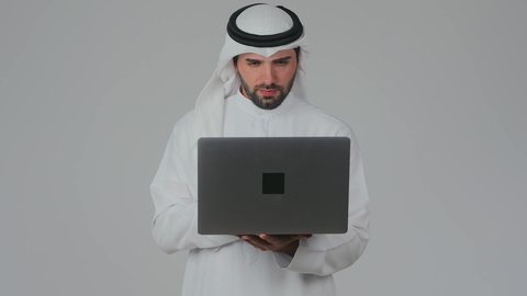 Managing and organizing business affairs remotely, integrating technology into practical life, using advanced modern technologies, skillful quick hands on the keyboard, a close-up portrait of an Emirati Gulf Arab man wearing a kandura and ghutrah working on a laptop, white background.