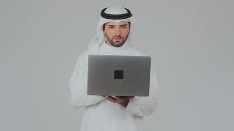 استخدام التقنيات الحديثة المتطورة، إدارة شؤون الأعمال وتنظيمها عن بعد، دمج التكنولوجيا في الحياة العملية، مهارة الايدي السريعة على لوحة المفاتيح، بورتريه مقرب لرجل عربي خليجي اماراتي يرتدي الكندورة والغترة يقوم بالعمل على الحاسب المحمول, خلفية بيضاء