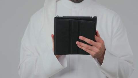استخدام التكنولوجيا والأجهزة الحديثة والمتطورة، دمج التقنية في الحياة اليومية، بورتريه مقرب لرجل عربي خليجي إماراتي يرتدي الكندورة والغترة يقف ويقوم بالنقر على جهاز التابلت، تصفح مواقع التواصل الاجتماعي عبر الانترنت، تطبيقات وبرامج الأجهزة اللوحية، خلفية بيضاء