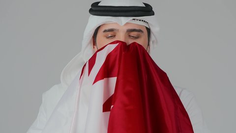 مناسبات واعياد وطنية، إحياء ذكرى تأسيس الدولة، الاحتفال باليوم الوطني القطري 18 ديسمبر، ثقافات وطنية و رموز, حب الوطن والانتماء إليه،  بورتريه مقرب لرجل عربي خليجي قطري يرتدي الثوب التقليدي والغترة يحمل علم قطر ويشمه بفخر واعتزاز،  خلفية بيضاء