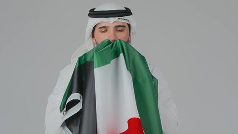 ايماءات الفخر والاعتزاز، الاحتفال باليوم الوطني الإماراتي, الأعياد و المناسبات الوطنية,  مفهوم الحب و الانتماء للبلاد, بورتريه مقرب لرجل عربي خليجي إماراتي يرتدي الكندورة والغترة البيضاء يقوم بحمل وشم علم الإمارات العربية المتحدة, خلفية بيضاء