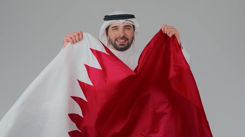 Gestures of pride and honor, national holidays and occasions, commemorating the founding of the state, celebrating Qatar National Day on December 18, national cultures and symbols, love for the homeland and belonging to it, a close-up portrait of a Qatari Gulf Arab man wearing traditional attire and a ghutrah holding the Qatari flag, white background.