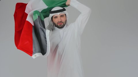 الأعياد و المناسبات الوطنية,، الاحتفال باليوم الوطني الإماراتي, الأعياد و المناسبات الوطنية, بورتريه مقرب لرجل عربي خليجي إماراتي يرتدي الكندورة والغترة البيضاء يقوم بوضع علم الإمارات العربية المتحدة على الاكتاف, إحياء ذكرى استقلال البلاد 1971 م، خلفية بيضاء
