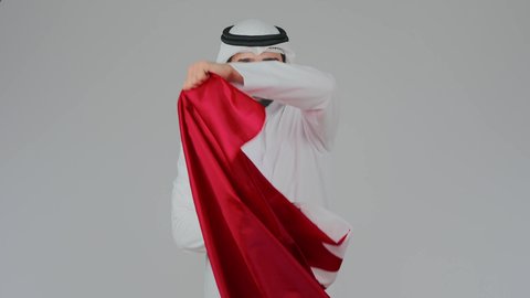 In the State of Qatar, there is pride and honor in heritage and culture, commemorating the founding of the state, celebrating Qatar National Day on December 18, national cultures and symbols, love for the homeland and belonging to it, a portrait of an Arab Gulf Qatari man wearing traditional attire and a bisht, draping the Qatari flag over his shoulders, with a white background.