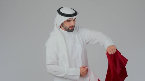 وضع العلم على الاكتاف دليل الانتماء الوطني، اعياد وطنية ومناسبات، إحياء ذكرى تأسيس الدولة، الاحتفال باليوم الوطني القطري 18 ديسمبر، حب الوطن والانتماء إليه،  بورتريه مقرب لرجل عربي خليجي قطري يرتدي الثوب التقليدي والغترة يحمل العلم القطري،  خلفية بيضاء