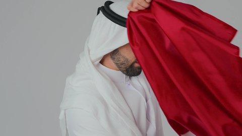 حمل العلم على الاكتاف دليل الانتماء الوطني، اعياد وطنية ومناسبات، إحياء ذكرى تأسيس الدولة، الاحتفال باليوم الوطني القطري 18 ديسمبر، حب الوطن والانتماء إليه،  بورتريه مقرب لرجل عربي خليجي قطري يرتدي الثوب التقليدي والغترة يحمل العلم القطري،  خلفية بيضاء