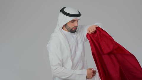 العلم على الاكتاف دليل الانتماء الوطني، اعياد وطنية ومناسبات، إحياء ذكرى تأسيس الدولة، الاحتفال باليوم الوطني القطري 18 ديسمبر، حب الوطن والانتماء إليه،  بورتريه مقرب لرجل عربي خليجي قطري يرتدي الثوب التقليدي والغترة يحمل العلم القطري،  خلفية بيضاء