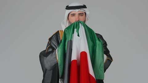 الاحتفال باليوم الوطني الإماراتي, الأعياد و المناسبات الوطنية,  مفهوم الحب و الانتماء للبلاد, بورتريه مقرب لرجل عربي خليجي إماراتي يرتدي الكندورة والغترة البيضاء يقوم بحمل وشم علم الإمارات العربية المتحدة بايماءات الفخر والاعتزاز, خلفية بيضاء