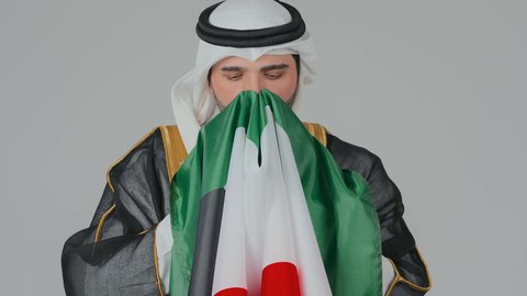 الاهتمام باليوم الوطني الإماراتي, الأعياد و المناسبات الوطنية,  مفهوم الحب و الانتماء للبلاد, بورتريه مقرب لرجل عربي خليجي إماراتي يرتدي الكندورة والغترة البيضاء يقوم بحمل وشم علم الإمارات العربية المتحدة بايماءات الفخر والاعتزاز, خلفية بيضاء