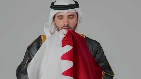 لقطة عن حب الوطن والانتماء العميق، إحياء ذكرى تأسيس الدولة، الاحتفال باليوم الوطني القطري 18 ديسمبر، ثقافات وطنية و رموز, حب الوطن والانتماء إليه،  بورتريه لرجل عربي خليجي قطري يرتدي الثوب التقليدي والبشت يحمل علم قطر ويشمه بفخر واعتزاز،  خلفية بيضاء