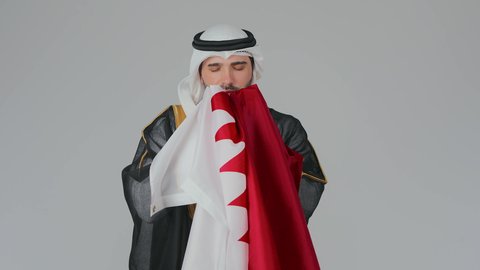 عن حب الوطن والانتماء العميق، إحياء ذكرى تأسيس الدولة، الاحتفال باليوم الوطني القطري 18 ديسمبر، ثقافات وطنية و رموز, حب الوطن والانتماء إليه،  بورتريه لرجل عربي خليجي قطري يرتدي الثوب التقليدي والبشت يحمل علم قطر ويشمه بفخر واعتزاز،  خلفية بيضاء