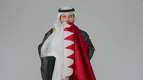 الولاء والانتماء الوطني لدولة قطر، إحياء ذكرى تأسيس الدولة، الاحتفال باليوم الوطني القطري 18 ديسمبر، ثقافات وطنية و رموز, حب الوطن والانتماء إليه،  بورتريه لرجل عربي خليجي قطري يرتدي الثوب التقليدي والبشت يحمل علم قطر ويشمه بفخر واعتزاز،  خلفية بيضاء
