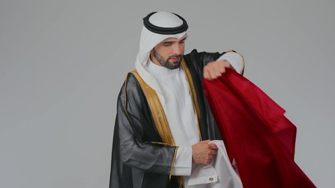 إحياء ذكرى تأسيس الدولة، الاحتفال باليوم الوطني القطري 18 ديسمبر، ثقافات وطنية و رموز, حب الوطن والانتماء إليه،  بورتريه لرجل عربي خليجي قطري يرتدي الثوب التقليدي والبشت يضع على اكتافه العلم القطر بايماءات الفخروالاعتزاز، حب الوطن والانتماء إليه،  خلفية بيضاء