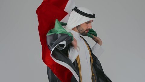 اليوم الوطني الاماراتي 2 ديسمبر، الاحتفال باليوم الوطني الإماراتي, الأعياد و المناسبات الوطنية,  مفهوم الحب و الانتماء للبلاد, بورتريه مقرب لرجل عربي خليجي إماراتي يرتدي الكندورة والغترة والبشت  يقوم بوضع علم الإمارات العربية المتحدة على الاكتاف, خلفية بيضاء