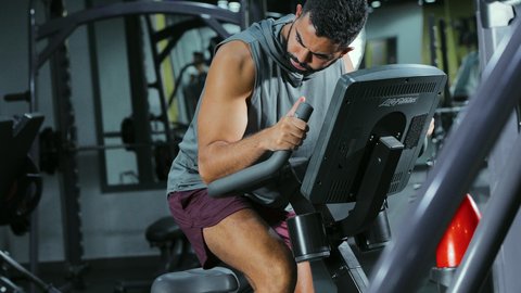 Improving heart health, stationary exercise bike, maintaining a healthy lifestyle, the concept of fitness and agility, activities and sports to strengthen muscles and nerves, a Saudi Arabian Gulf man wearing sportswear exercising on a stationary bike