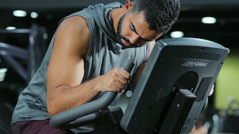 Reducing muscle stiffness, maintaining a healthy lifestyle, the concept of agility and physical fitness, activities and sports to strengthen muscles and nerves, an Arab Gulf Saudi man wearing sportswear exercising on an exercise bike
