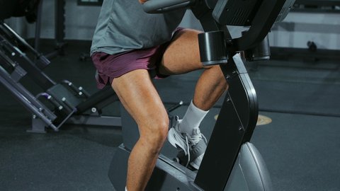 Regular exercise, using a stationary bike, maintaining a healthy lifestyle, activities and sports to strengthen muscles and nerves, a close-up of an Arab Gulf Saudi man wearing sportswear exercising at a gym