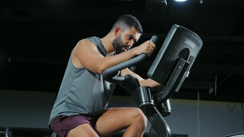 تنشيط عضلات الساقين والفخذين, قضاء وقت ممتع على العجلة الهوائية، المحافظة على نظام الحياة الصحي، انشطة ورياضات لتقوية العضلات و الاعصاب، رجل عربي خليجي سعودي يرتدي الملابس الرياضية يتمرن في النادي الرياضي