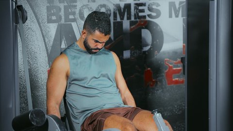 Developing leg strength, focusing on health and fitness, using exercise equipment: A young Saudi Arabian man wearing sportswear exercises on a leg exercise machine at the gym; a healthy lifestyle; maintaining physical balance.