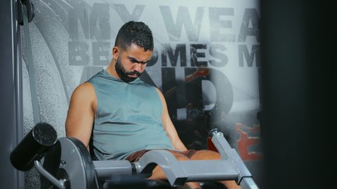 زيادة قوة الساقين, الاهتمام بالصحة و الرشاقة, استخدام الأجهزة الرياضية، شاب عربي خليجي سعودي يرتدي الزي الرياضي يتمرن على جهاز تمارين الارجل في الجيم، أسلوب حياة صحي، المحافظة على التوازن الجسدي