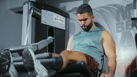 بناء القوة بشكل متوازن, تحكم العضلات في الوزن, الاهتمام بالصحة و الرشاقة, استخدام الأجهزة الرياضية، شاب عربي خليجي سعودي يرتدي الزي الرياضي يتمرن على جهاز تمارين الارجل في الجيم، أسلوب حياة صحي