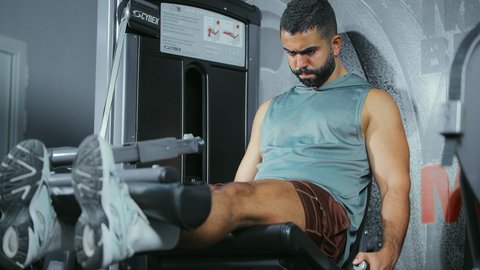Strengthening and building body muscles, focusing on health and fitness, using exercise equipment, a young Saudi Arabian man wearing sportswear exercises on a leg exercise machine at the gym, a healthy lifestyle, maintaining physical balance