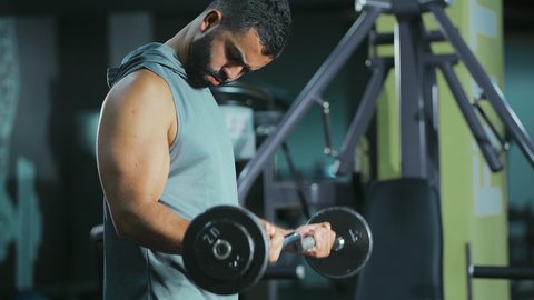 مراقبة انقباض و انبساط العضلة, التدرب على إتقان رفع الاوزان، اتباع نظام صحي، نشاط بدني للمحافظة على اللياقة الجسدية، شاب عربي خليجي سعودي يقوم بأداء التمارين باستخدام البار, رياضة كمال الأجسام، ايماءات القوة و الثقة