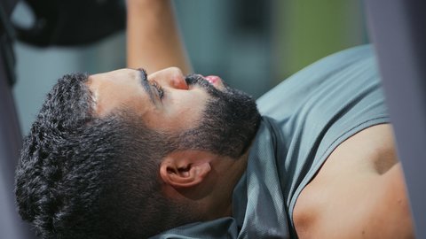 القوة والتحفيز وبناء العضل، النظر و التركيز في شيء ما، مفهوم الرشاقة واللياقة البدنية, رياضة كمال الأجسام، استخدام الاثقال الرياضية، شاب عربي خليجي سعودي يرتدي الزي الرياضي يقوم بممارسة تمارين رفع الأوزان، تقوية الأعصاب والعضلات