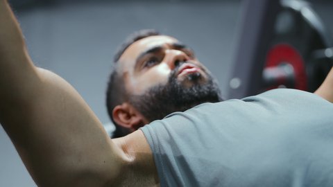 النظر و التركيز في شيء ما، مفهوم الرشاقة واللياقة البدنية, رياضة كمال الأجسام، استخدام الاثقال الرياضية، شاب عربي خليجي سعودي يرتدي الزي الرياضي يقوم بممارسة تمارين رفع الأوزان، تقوية الأعصاب والعضلات