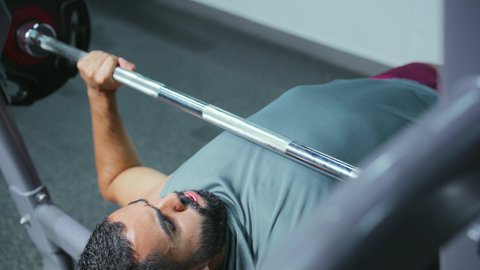 التمرن داخل النادي الرياضي,  إيماءات القوة والثقة, الاهتمام بالصحة واللياقة الجسدية، رياضة كمال الأجسام، استخدام الاثقال الرياضية، شاب عربي خليجي سعودي يرتدي الزي الرياضي يقوم بممارسة تمارين رفع الأوزان، تقوية الأعصاب والعضلات