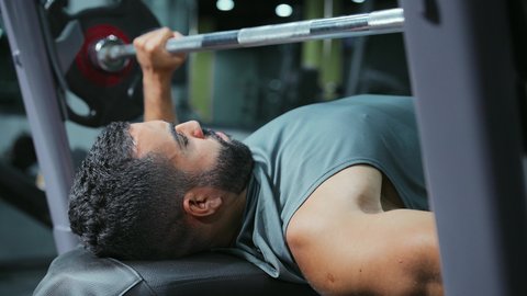 قضاء الوقت في ممارسة الرياضة,  إيماءات القوة والثقة, الاهتمام بالصحة واللياقة الجسدية، رياضة كمال الأجسام، استخدام الاثقال الرياضية، شاب عربي خليجي سعودي يرتدي الزي الرياضي يقوم بأداء تمارين رفع الأوزان، تقوية الأعصاب والعضلات