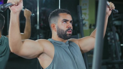 حرق الدهون وتقليل الوزن، نشاط لتقوية العضلات، الاهتمام بالصحة و الرشاقة, استخدام الأجهزة الرياضية، شاب عربي خليجي سعودي يرتدي الزي الرياضي يقوم بممارسة تمارين الظهر على آلة السحب العلوي