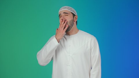 تعابير النعاس والحاجه الى النوم، بورتريه لرجل عربي خليجي اماراتي يرتدي الكندورة والطاقية يرفع يديه بإيماءات النعاس, الإحساس بالتعب والتثاؤب ,مفهوم الكسل والخمول، خلفيه ملونة