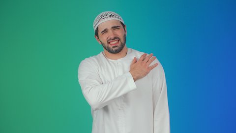 الحاجه لوضع خطة علاجية, طلب المساعده للذهاب الى المستشفى، الإحساس بالتعب والإرهاق, إيماءات الألم في الجسد، التهاب العضلات والمفاصل، بورتريه لرجل عربي اماراتي خليجي يرتدي الكندورة والقبعة البيضاء يضع يده على كتفه بتعابير الوجع، خلفية ملونة
