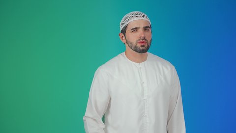 الانصات وحسن الاستماع، بورتريه لرجل عربي خليجي اماراتي يرتدي الكندورة والقبعة البيضاء يضع يده خلف أذنه بإيماءات التنصت والتجسس، التركيز على الكلام وسماع الاسرار، خلفية ملونة