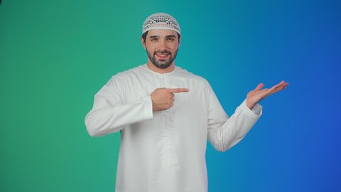 استخدام حاسة اللمس لتحريك العناصر الهولوجراميه، بورتريه لرجل عربي خليجي اماراتي يرتدي الكندورة والقبعة البيضاء يشير الى يده، ايماءات حمل ورفع شيء ما، الإشارة نحو هدف معين، خلفية ملونة